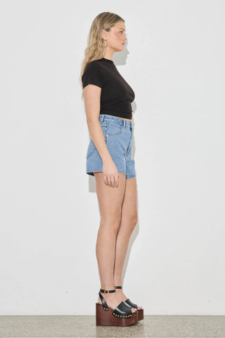 Woman wearing a black top and denim shorts standing against a white background