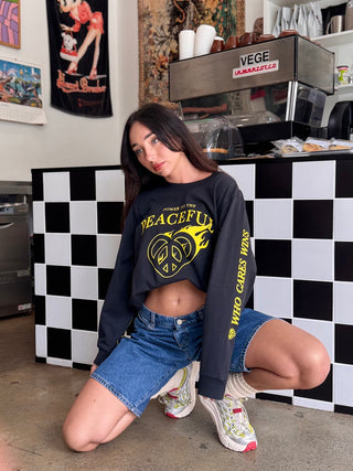 Woman wearing a black 'PEACEFUL' sweatshirt with yellow text in a casual setting.
